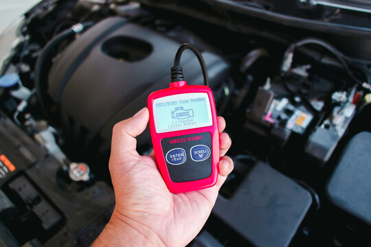 OBD2 or OBD scanner in a auto mechanic hand for engine system analysis with engine compartment blurred on background , Car maintenance service concept
