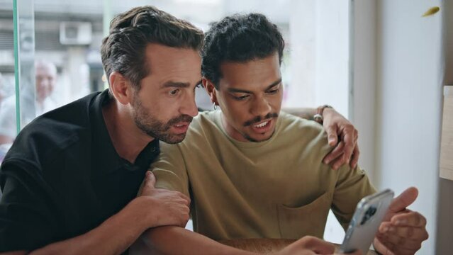 Homosexual partners watching cellphone screen sitting modern cafe close up. 