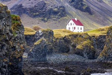 Arnarstapi, Iceland. A view of the craggy coastline with a solitary house. Autumn colours with mountains in the background. Snaefellsnes peninsula.