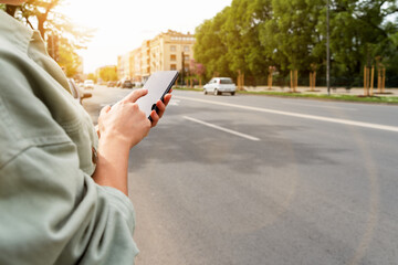 Urban woman person stands next to road in city and using her smartphone. Searching car rental,...