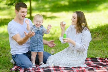 Happy family playing with soap bubbles during a picnic in nature on a warm sunny day, smiling,...