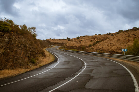 Carretera asfaltada con curvas y mojada por la reciente lluvia otoñal. Carretera rural HU-4401 en el km 14 un día de lluvia en Sanlúcar de Guadiana, Andalucía, España.