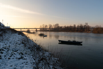 Anchored boats in river during sunset against bridge in haze, winter landscape