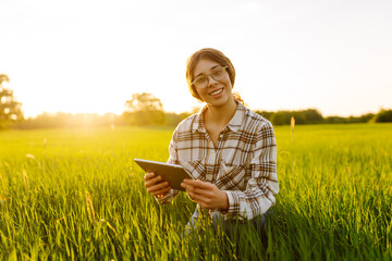 Young Woman Farmer on a green wheat field with a tablet in his hands. Smart farm. The concept of...