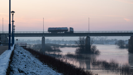 Truck driving across bridge during twilight, bridge across Sava river in Brod during winter