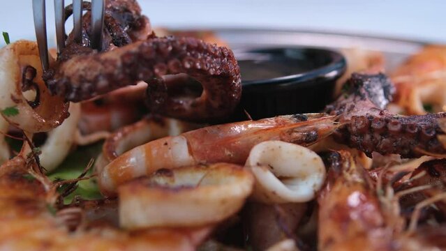 Cropped unrecognizable person with tasty fried octopus tentacles on tongs served in bowl with white sauce on table against. gray background Soy sauce