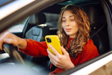 Young woman is driving a car with phone. Leisure, travel, technology, navigation.