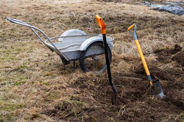 A wheelbarrow and shovel rest in the dirt of a grassy field