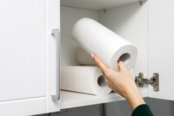 housewife takes out a roll of paper towel from the kitchen cabinet.