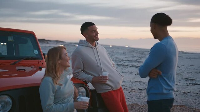 Young couple with friends on vacation standing by car at beach watching morning sunrise and drinking coffee on road trip  - shot in real time