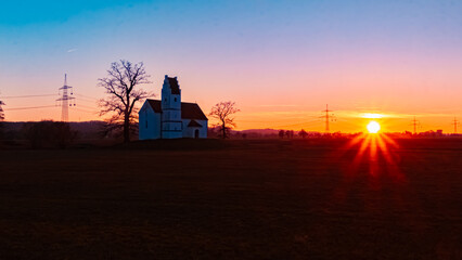 Fototapeta premium Sunset with a church silhouette and a sunstar at Huett, Eichendorf, Dingolfing-Landau, Bavaria, Germany