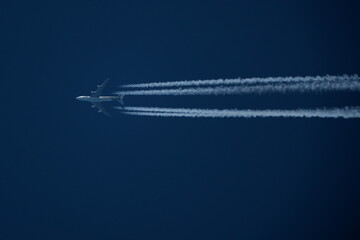 Airplane in the blue sky with contrails in the air.