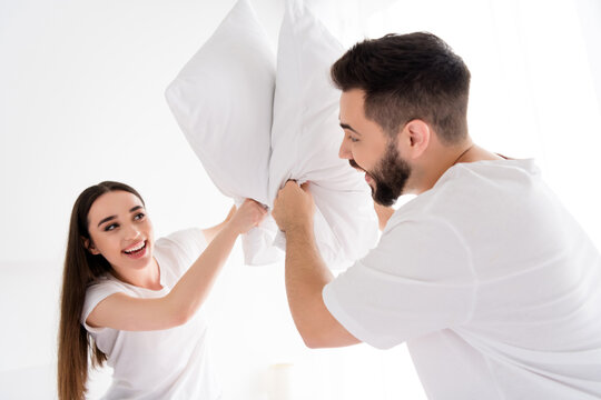 Photo of excited funky husband wife nightwear fighting pillows having fun indoors house bedroom