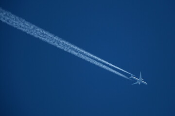 Airplane in the blue sky with contrails in the air.
