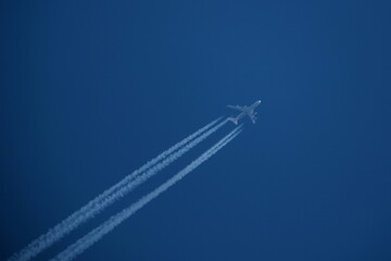 Airplane in the blue sky with contrails in the air.