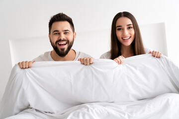Photo of positive couple girl guy hold white blanket bed in morning room