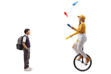 Naklejka premium Surprised schoolboy standing and watching a female riding a mono cycle and juggling