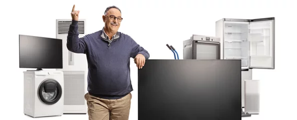  Mature man pointing up and standing next to a flat tv screen and other home electric appliances © Ljupco Smokovski