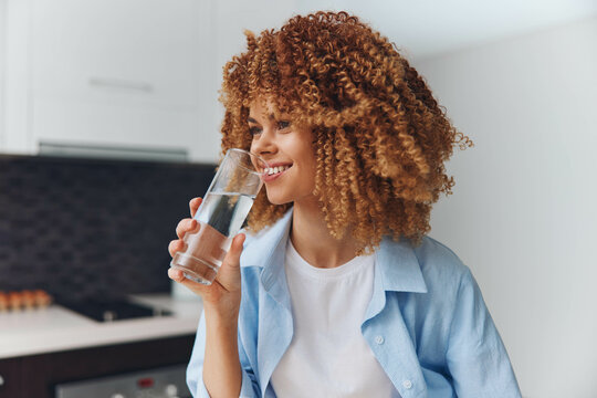 Fototapeta Young African American woman enjoying a refreshing drink of water in her stylish kitchen at home