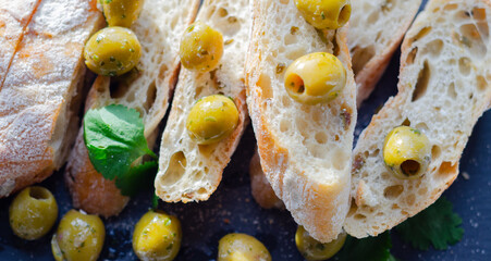 Baguette stuffed with olives, cut with fresh green olives and parsley, served on a stone plate