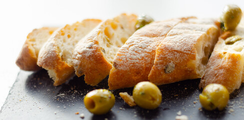Baguette stuffed with olives, cut with fresh green olives and parsley, served on a stone plate
