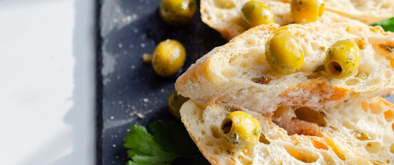 Baguette stuffed with olives, cut with fresh green olives and parsley, served on a stone plate