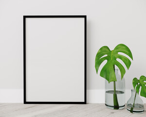 Blank vertical black poster frame standing on light wooden floor with next to white wall. Blank poster frame mockup. Empty picture frame mockup. Vertical frame mock up. Blank photo frame. 3d rendering