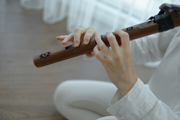 Beautiful young curly woman playing a wooden flute at home near the window © Alina