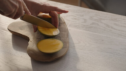 Man cutting ripe mango on olive board on white oak table