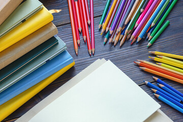 Colorful colored pencils, stack of books and open sketchbook on dark rustic table. Copy space