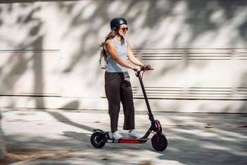 Confident cheerful woman riding electric push scooter through the city