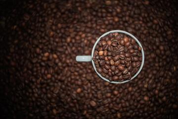 Coffee beans in a white cup on coffee beans background.