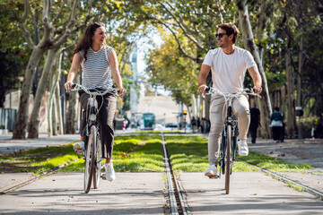 Shot of happy loving couple cycling while looking each other in the city - 790066354