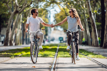 Happy loving couple cycling while holding each other hand in the city