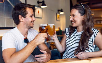 Pretty young couple toasting with beer while looking each other at the bar