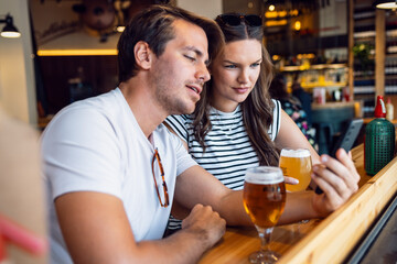 Pretty young couple drinking beer while using smartphone the bar
