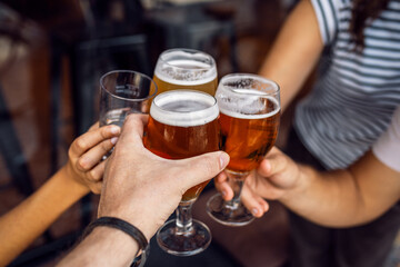 Hand's of young friends toasting with beer while having fun in a restaurant.
