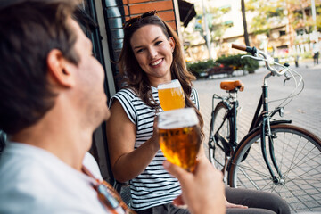 Pretty young couple toasting with beer while looking each other on a bar terrace