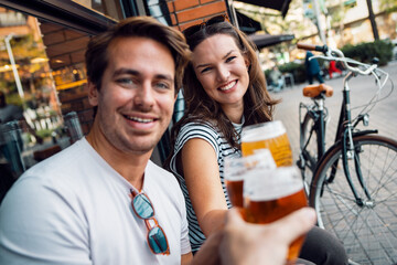 Pretty young couple toasting with beer while looking each other on a bar terrace - 790067198