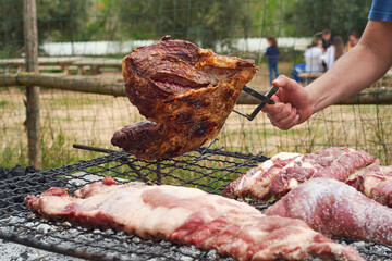 A hand turns half-grilled meat from a family barbecue with friends in the background.