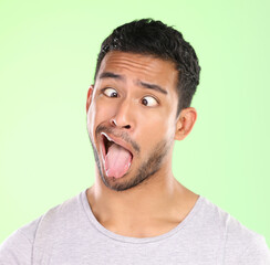 Man, crosses eyes and tongue in studio, silly and goofy comic or funny face on green background. Male person, mockup space and emoji for joke or comedy humor, student and quirky or crazy character