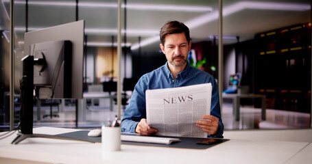 Businessman Reading Newspaper At Office Desk
