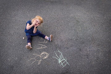 little girl draws with chalk on the asphalt in summer