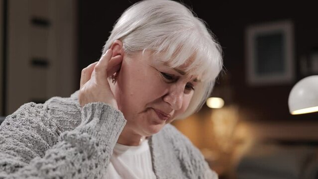 Earache. Senior woman suffers from otitis media and ear inflammation. Close-up of face of elderly woman who is touching and scratching her ear