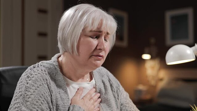 Chest pain, hysteria. Senior woman with pain in chest and suffers, crying from physical or mental pain. Close-up of elderly woman in despair having heart attack, panic or severe stress and depression