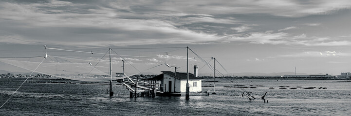Tranquil waters embrace a picturesque scene of fishing boats and rustic huts along the shores of Pialassa dei Piomboni, near Ravenna
