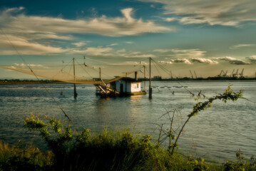 Tranquil waters embrace a picturesque scene of fishing boats and rustic huts along the shores of...