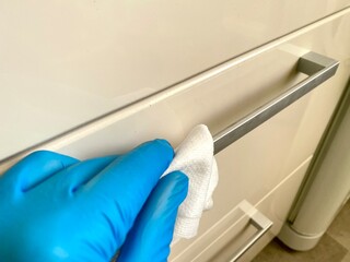 Gesture of cleaning an electric blue cabinet handle with blue gloves and a cloth