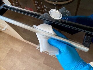 Person in electric blue gloves cleans oven with cloth