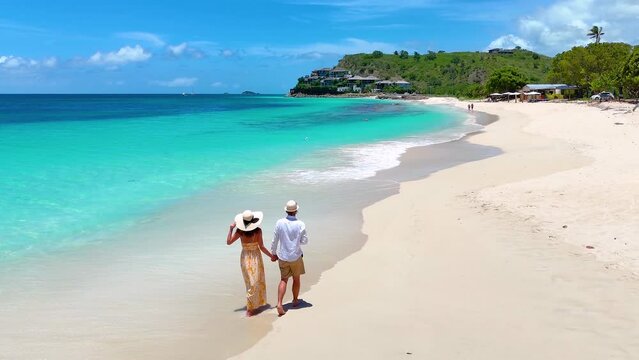 Elevated view of a couple walking down the beuatiful Darkwood beach with turquoise sea in the Caribbean, Antigua and Barbuda islands